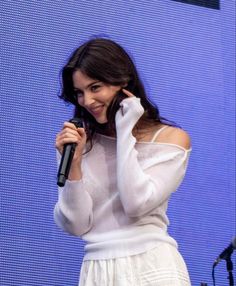 a woman holding a microphone up to her ear while standing in front of a screen