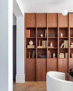 a living room filled with lots of wooden bookshelves next to a white chair