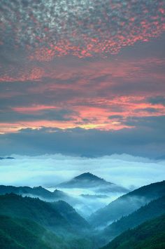 the sun is setting over mountains with fog in the valleys and hills below it, as seen from an overlook point