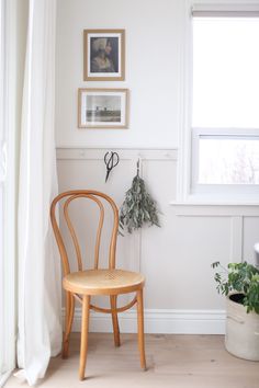 a chair sitting in front of a window next to a potted plant and pictures on the wall