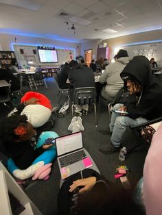 several people sitting in chairs with laptops on their laps and one person wearing a hoodie