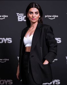 a woman standing in front of a black background wearing a white crop top and black blazer