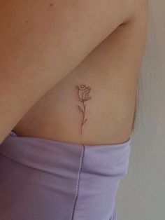 a woman's stomach with a single flower tattoo on her left side ribcage