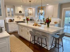 a kitchen with white cabinets and an island in the middle, surrounded by bar stools