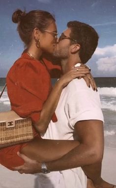 a man and woman kissing on the beach while holding a wicker basket in front of them