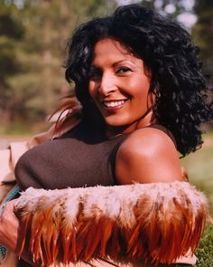 a woman laying in the grass with her arm around an animal's leg and smiling