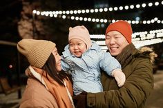 two adults and a child are smiling at each other in front of some christmas lights