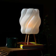 a white lamp sitting on top of a wooden table next to a book and cup