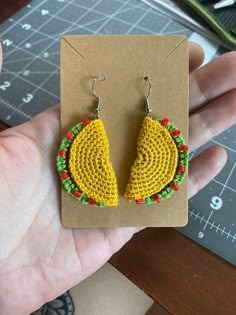 a hand holding a pair of yellow and green crocheted earrings on top of a piece of cardboard