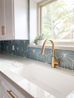 a kitchen sink with a gold faucet next to a window and white cabinets