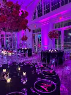 a room filled with tables and chairs covered in purple lighting next to tall vases full of flowers