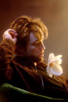 a man holding a flower in his right hand and looking off into the distance with light shining on him