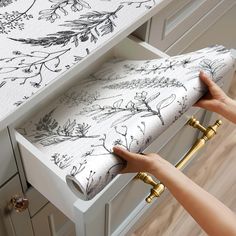 a woman is opening the drawers in her kitchen with floral wallpaper and gold handles