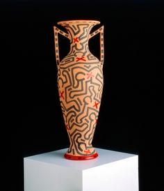 an old vase with designs on it is sitting on a white pedestal in front of a black background