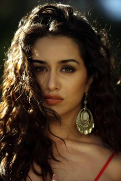 a close up of a woman with long hair and earrings on her head, looking at the camera