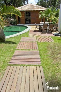 a wooden walkway leading to a pool in the middle of a yard with chairs and tables