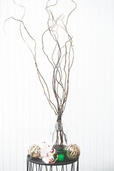 a vase filled with branches and flowers on top of a black table next to a white wall