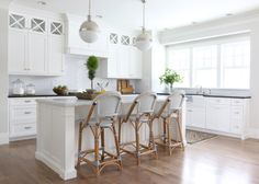 a kitchen with white cabinets and wooden flooring has bar stools in front of the island