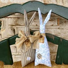 two stuffed bunnies sitting on top of a wooden bench next to a brick wall