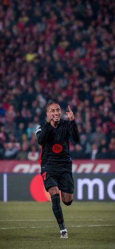 a soccer player running on the field with his hand up in the air and mouth open