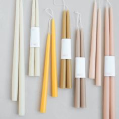 several different colored candles are lined up on a white surface with tags attached to them