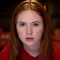 a close up of a person wearing a red shirt and looking at the camera with a serious look on her face