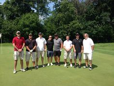 a group of men standing next to each other on a green golf course with trees in the background