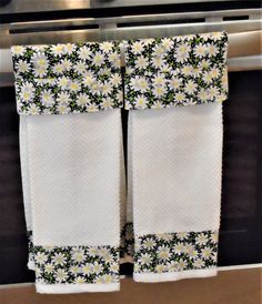 two white towels hanging from the side of an oven with daisies and leaves on them