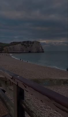 people are walking on the beach at night with dark clouds in the sky above them