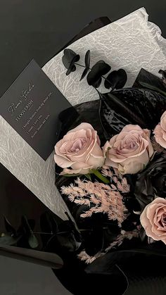 a bouquet of pink roses sitting on top of a black and white table cloth next to an envelope