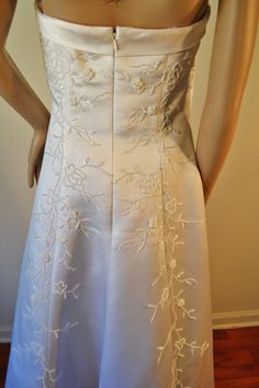 the back of a white wedding dress with embroidered flowers and leaves on it's waist