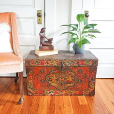 an old trunk is sitting on the floor next to a chair and a potted plant