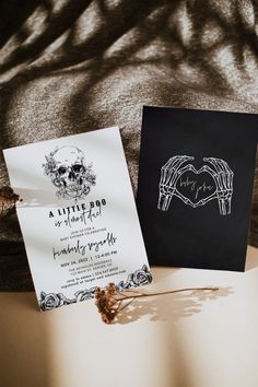 two wedding cards sitting on top of a bed next to each other, one with a skull and the other with hands