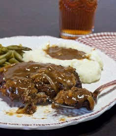 a white plate topped with meat and gravy next to mashed green beans