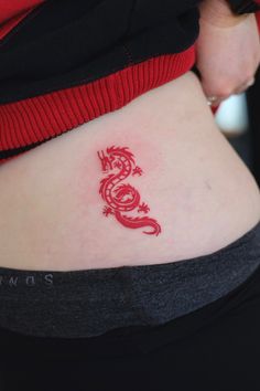 a woman's stomach with a red dragon tattoo on her side ribcage