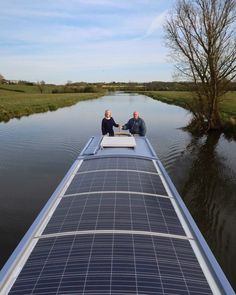 two people sitting on the back of a solar powered boat in a body of water