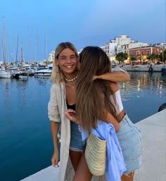 two women are hugging each other by the water in front of some boats and yachts