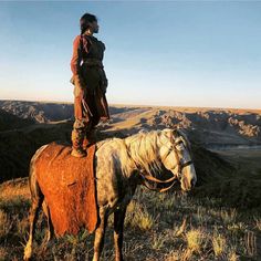 a man riding on the back of a horse in a field next to a valley