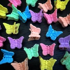 there are many different colored plastic butterflies on the black table and one is yellow, pink, blue, green