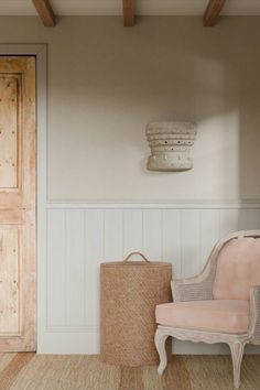 a pink chair sitting in front of a wooden door next to a basket on the floor