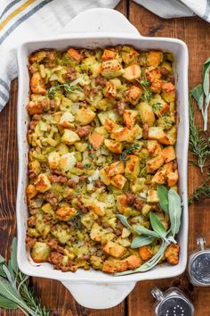 a casserole dish filled with stuffing and vegetables on top of a wooden table