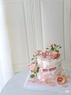 a three tiered cake with pink flowers and leaves on the top is sitting on a white table