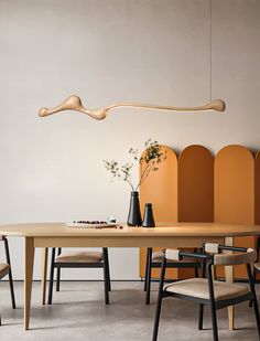 a wooden table with chairs and vases on it in front of a white wall