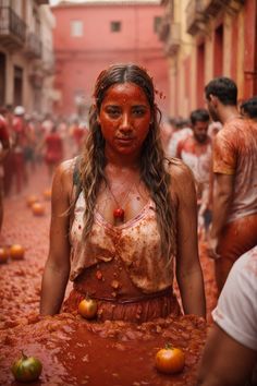 a woman covered in red paint surrounded by other people and oranges on the ground