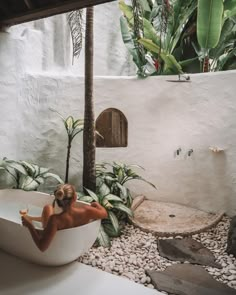 a woman sitting in a bathtub surrounded by rocks and greenery, while holding a banana