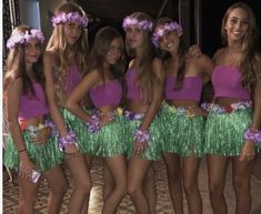 a group of young women standing next to each other wearing purple and green skirts with flowers in their hair