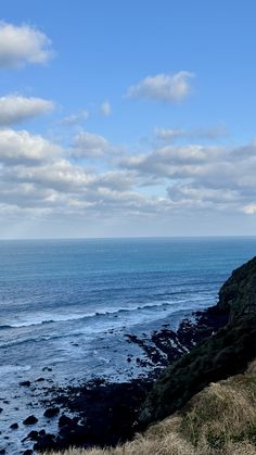 a bench sitting on the side of a cliff overlooking the ocean with clouds in the sky