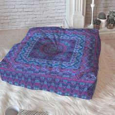 a purple and blue blanket sitting on top of a white fur covered floor next to a fireplace