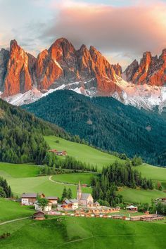 the mountains are covered in snow and green grass, with small houses on each side