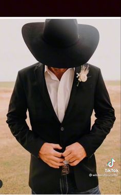 a man in a black suit and cowboy hat with his hands on his hips looking down